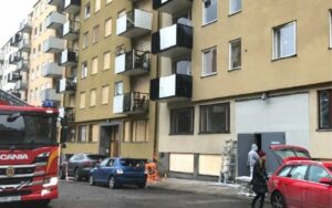 Hyreshuset på Gyllenstiernsgatan med tillfälligt gråa dörrar i porten, och en fastighet tillhörande en brf intill bakom, med fönsterskydd i trä. Foto: Linda Myrin