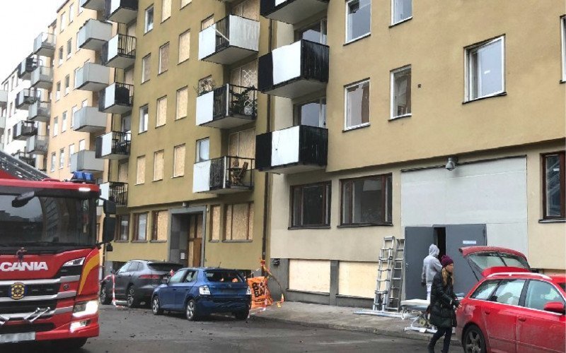 Hyreshuset på Gyllenstiernsgatan med tillfälligt gråa dörrar i porten, och en fastighet tillhörande en brf intill bakom, med fönsterskydd i trä. Foto: Linda Myrin