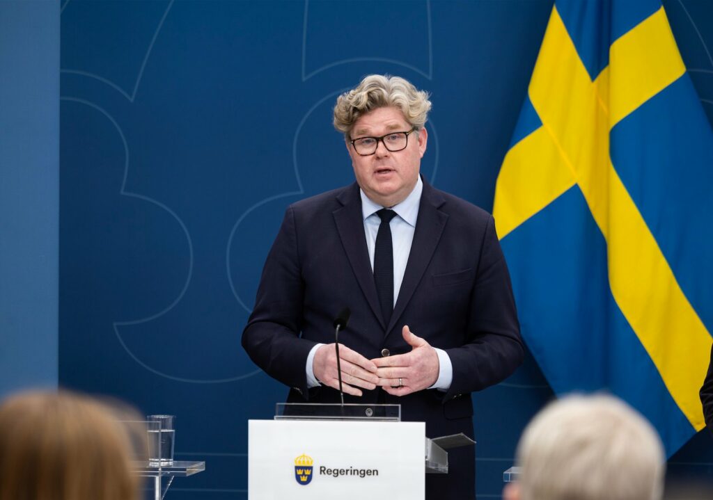 Justitieminister Gunnar Strömmer håller presskonferens vid talarpodium med svenska flaggan i bakgrunden