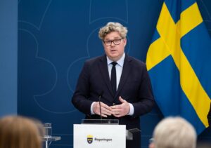 Justitieminister Gunnar Strömmer håller presskonferens vid talarpodium med svenska flaggan i bakgrunden